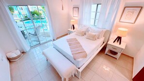 A hotel room with a bed, bedside tables, a bench, and a view of a pool.