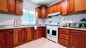 A kitchen with wooden cabinets, a gas stove, a microwave, and a window providing natural light. - Pool View, Walk to Beach, Shops, Dining, Fast Wifi (Punta Cana)