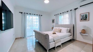 A bedroom with a bed, a television, and a window with curtains. - Pool View, Walk to Beach, Shops, Dining, Fast Wifi (Punta Cana)