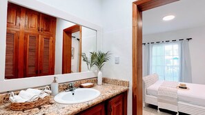 A bathroom with a sink, mirror, wooden cabinets, and a potted plant. - Pool View, Walk to Beach, Shops, Dining, Fast Wifi (Punta Cana)