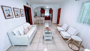 A spacious living area with a sofa, two armchairs, a coffee table, and a dining area in the background.