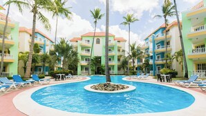 A resort with a central swimming pool surrounded by lounge chairs and palm trees. - Pool View, Walk to Beach, Shops, Dining, Fast Wifi (Punta Cana)