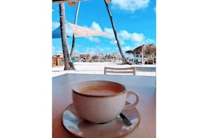 A cup of coffee on a table with a view of a beach and palm trees.