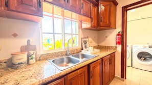 A kitchen with wooden cabinets, a double sink, a window with a view, and a washing machine.