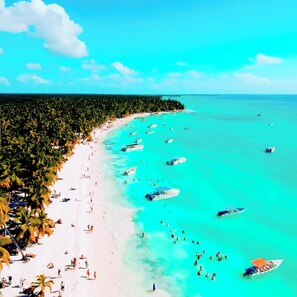 A beach with clear turquoise waters, boats, and palm trees.