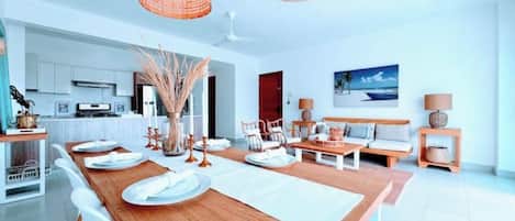 A modern kitchen with white cabinets, a wooden dining table set with plates, and a hanging light fixture.