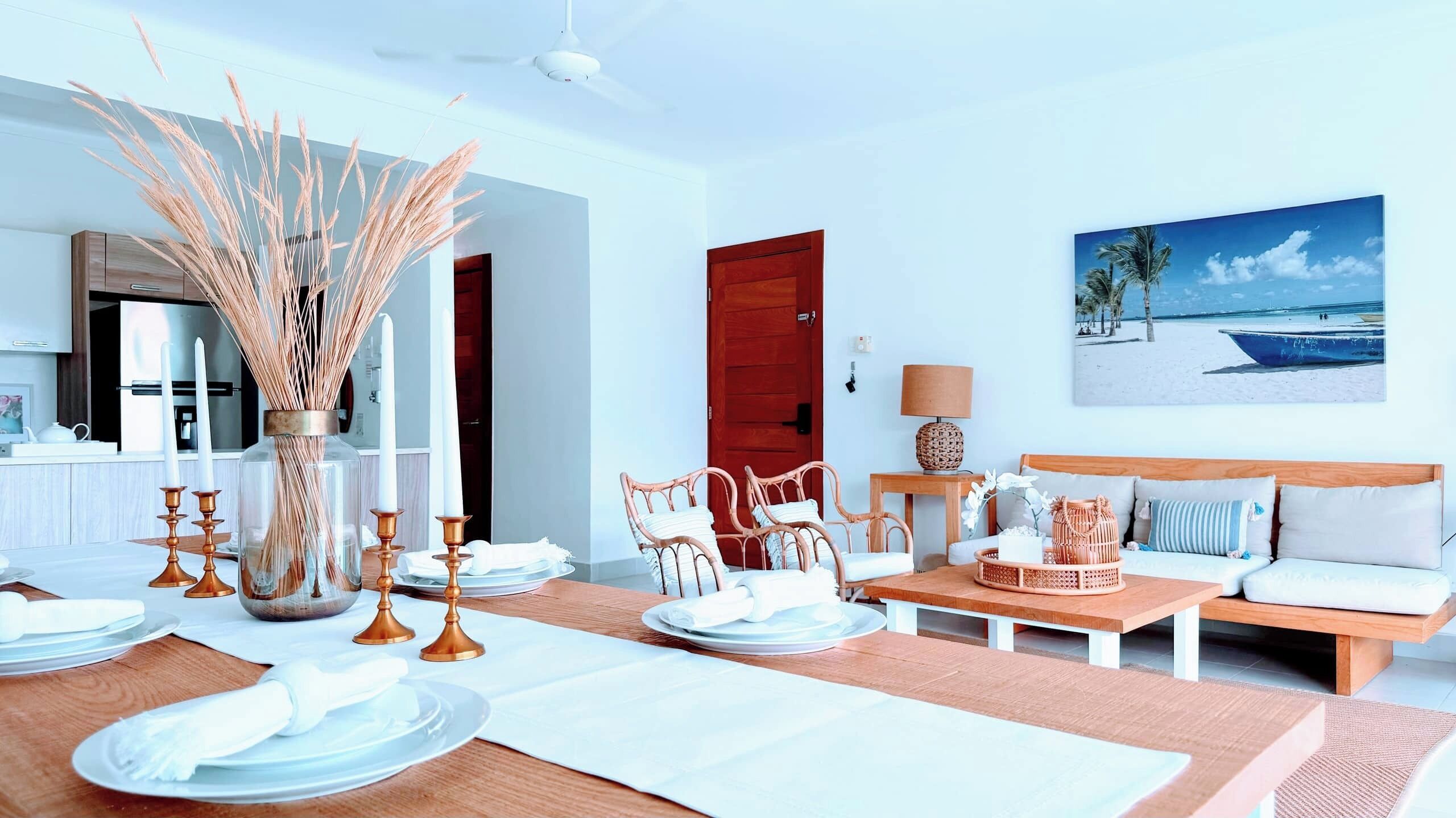 A modern living room with a dining area, a wooden door, and a beach-themed painting on the wall.