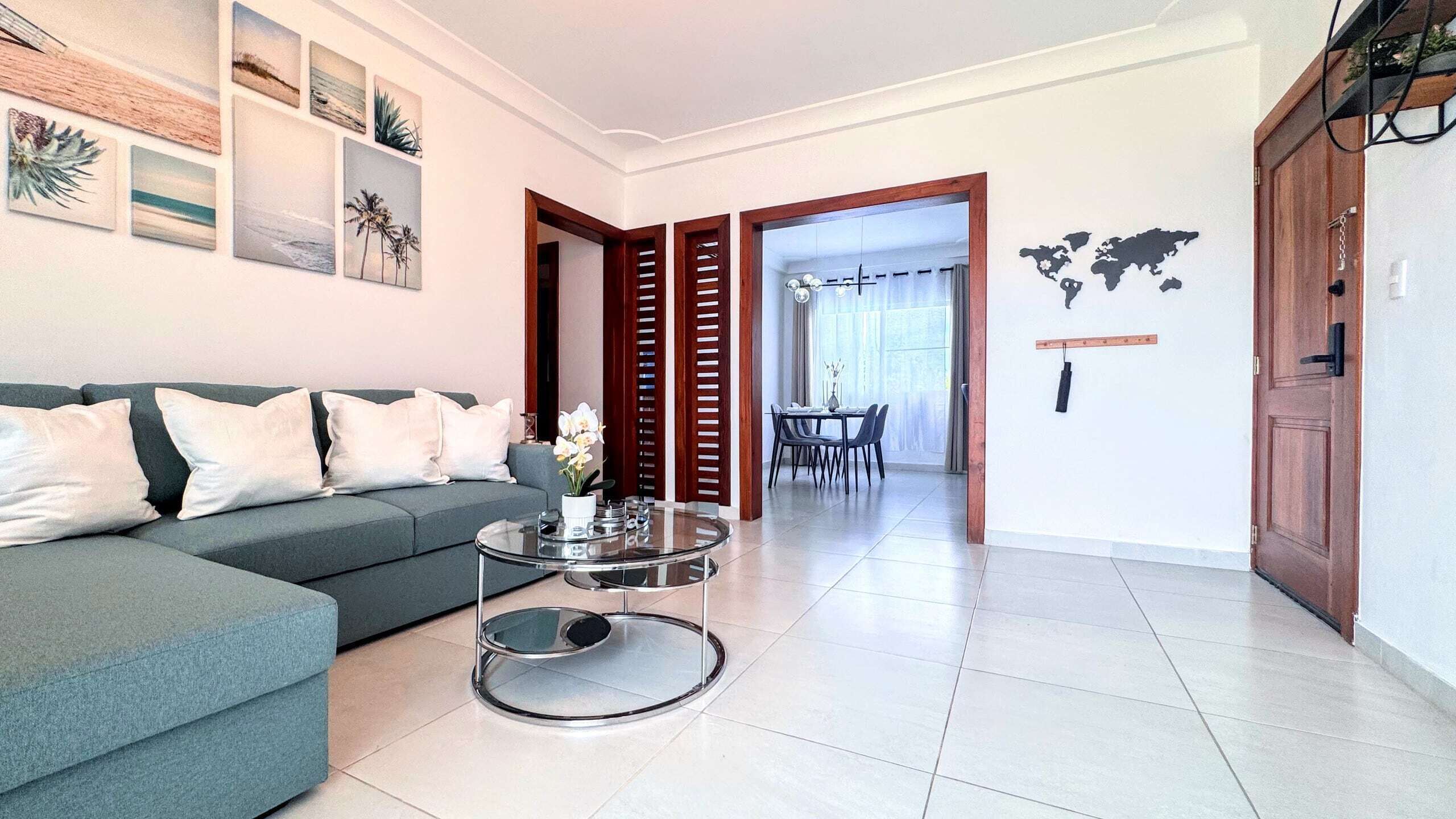 A modern living room with a grey sofa, a glass coffee table, and a dining area with a table and chairs.