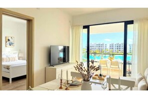 Une chambre d’hôtel avec un lit, une télévision, une table à manger décorée de bougies et un balcon donnant sur la piscine.