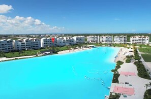 A large swimming pool with a clear blue water, surrounded by a resort area with multiple buildings.