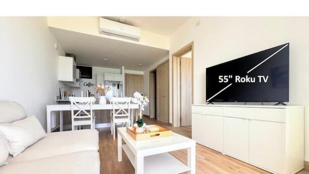Een moderne woonkamer met een witte bank, een salontafel en een 55 inch Roku TV bevestigd aan een witte kast.