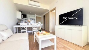 A modern living room with a white sofa, a coffee table, and a 55" Roku TV mounted on a white cabinet.