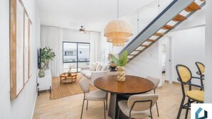 A modern living room with a dining area, a staircase, and a large window.