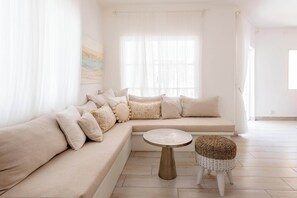 Un salon moderne avec un canapé d’angle beige, une table basse ronde et un tabouret en osier.