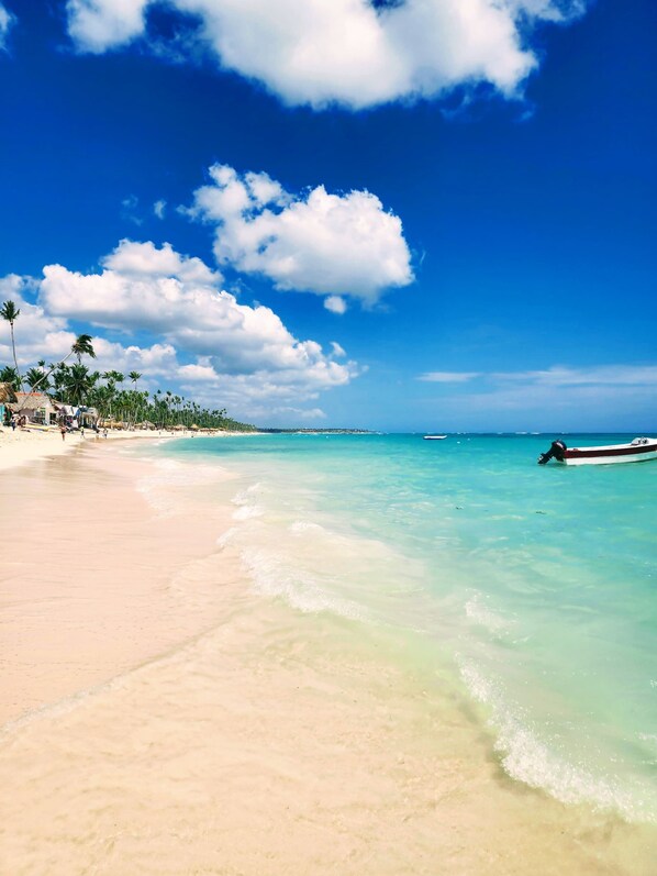 A beach with clear turquoise water, a boat on the shore, and palm trees lining the beach.