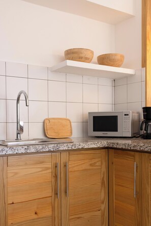A kitchen with a stainless steel faucet, a microwave, a wooden cutting board, and two wooden bowls on a white shelf.