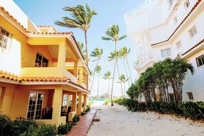 A hotel corridor with multiple balconies, palm trees, and a sandy path.