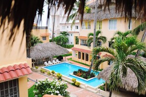 A pool area with a thatched roof, surrounded by palm trees and a poolside lounge. - Steps 2 Beach w Loungers, Pool-view, Priv Rooftop (Punta Cana)