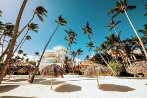 Een resort met palmbomen, rieten zonneschermen en een gebouw met balkons.