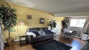 A living room with a sofa, a dining table with chairs, a black rug, and a potted plant. - Location location location ! (Lakewood)