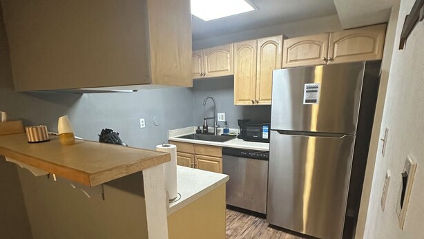 A compact kitchen with wooden cabinets, a stainless steel refrigerator, and a built-in island with a sink. - Location location location ! (Lakewood)