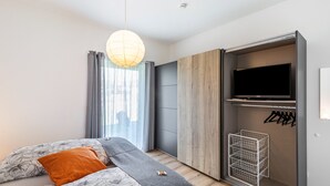 Een moderne slaapkamer met een bed, een hanglamp, een kledingkast en een televisietoestel.