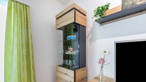 Een kamer met een glazen kast, een flatscreen televisie, een houten kast en een groen patroon gordijn.