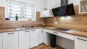 Een moderne keuken met witte kasten, een houten aanrecht, een zwarte magnetron en een raam met gordijnen.