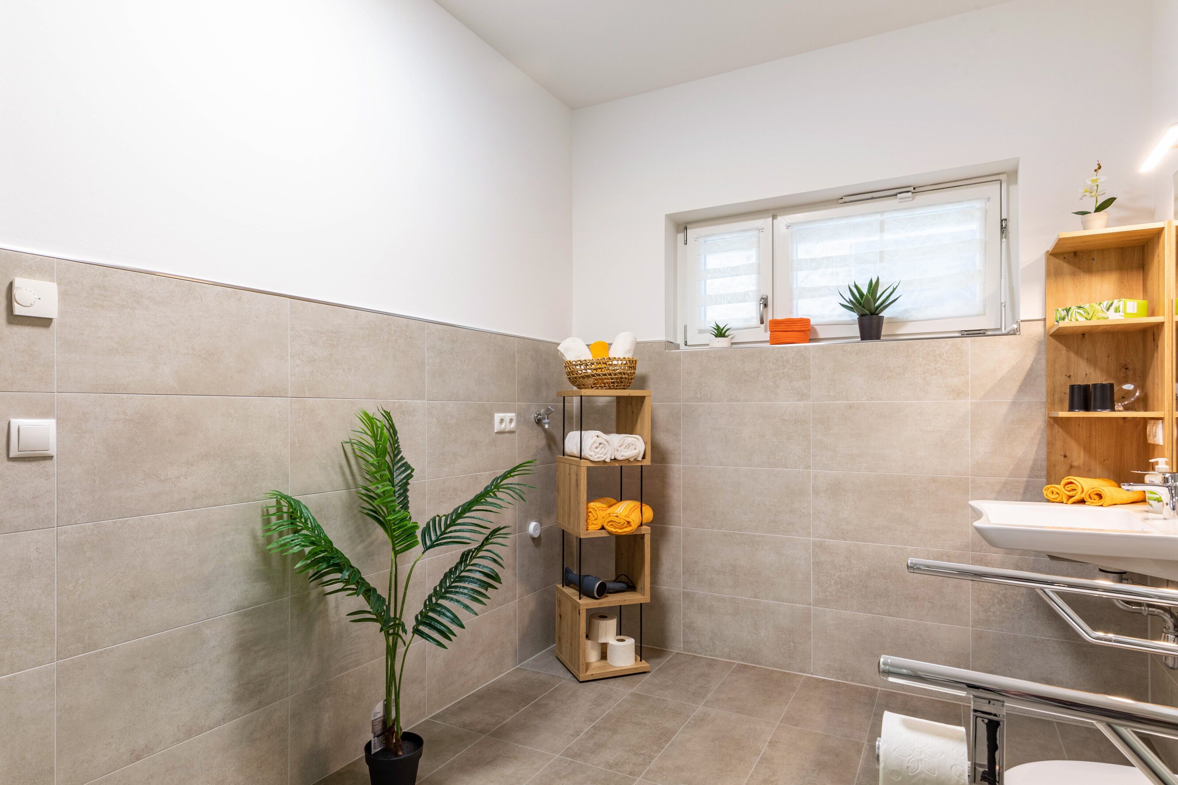 Une salle de bain moderne équipée d’une douche, d’un lavabo, d’une fenêtre et d’une étagère où sont rangées les serviettes et les articles de toilette.