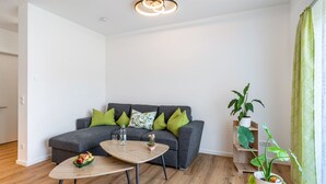 Een moderne woonkamer met een grijze bank, groene kussens, een houten salontafel en een potplant.