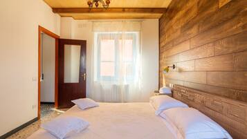 Ein Schlafzimmer mit einem hölzernen Kopfteil, einem Bett mit weißer Bettwäsche, einem Fenster mit durchscheinenden Vorhängen und einer Pendelleuchte.