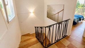 Een trap met een zwarte leuning, een schilderij aan de muur en een bed met een blauwe spreidek in de achtergrond.