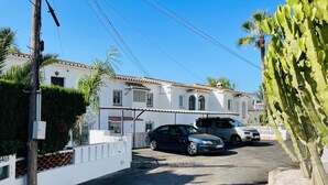 A residential street with parked cars, a white building with a tiled roof, and a cactus plant. - Costabella Beach House · Magnolia Marbella (Marbella)