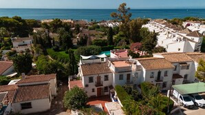 A coastal residential area with terracotta-tiled buildings, a clear view of the sea, and lush greenery. - Costabella Beach House · Magnolia Marbella (Marbella)