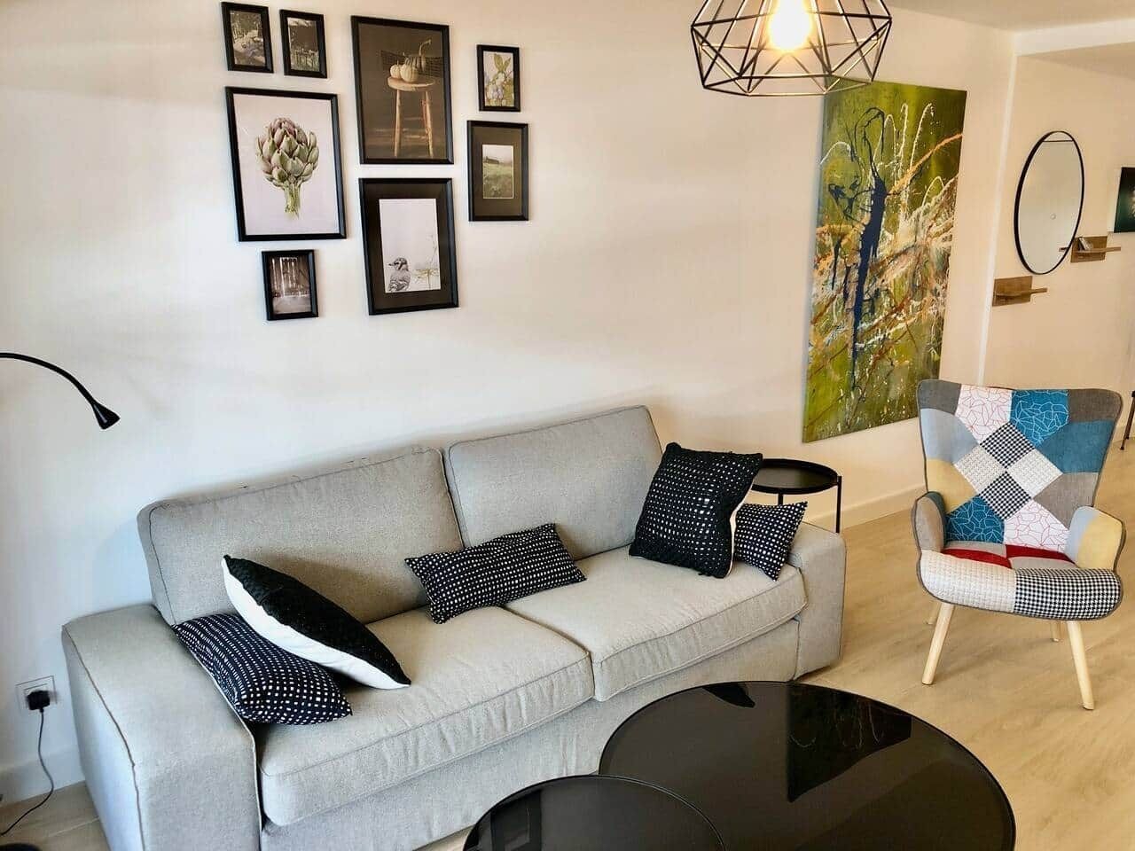 A modern living room with a grey sofa, black and white patterned cushions, a black coffee table, and a colorful armchair.