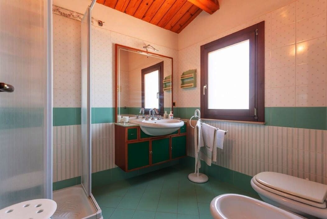 A bathroom with a wooden ceiling, a large mirror, a sink, a toilet, and a shower.