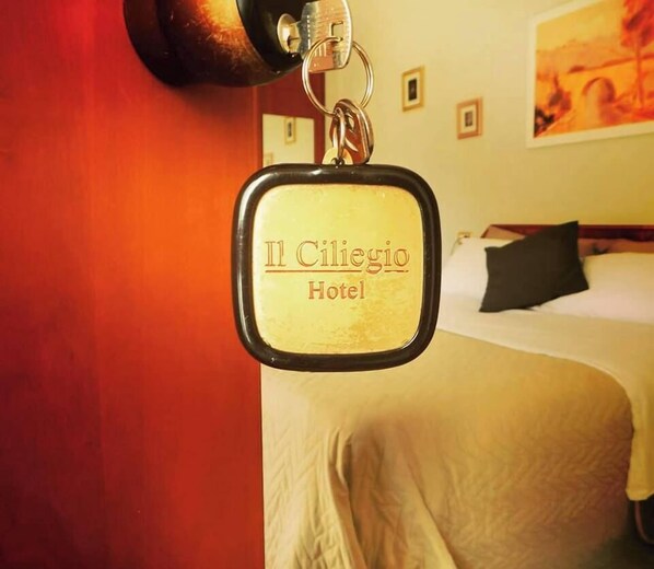 A keychain with "Il Ciliegio Hotel" text, a bed, and a painting on the wall. - Hotel Il Ciliegio (Santo Stefano del Sole)