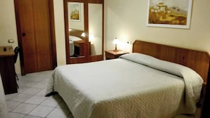 A hotel room with a bed, a wooden headboard, a bedside table with a lamp, a mirror, and a door. - Hotel Il Ciliegio (Santo Stefano del Sole)
