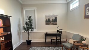 Quarto com escrivaninha de madeira, uma cadeira, estante de livros, planta em vaso e tapete estampado.