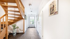 A hallway with a wooden staircase, a vase with plants, and a door at the end. - Holiday Home 'Großes Im Grünen -' with Private Terrace, Private Garden and Wi-Fi (Dummerstorf)
