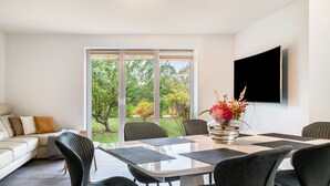 A modern dining area with a glass table, black chairs, and a large window with a view of greenery. - Holiday Home 'Großes Im Grünen -' with Private Terrace, Private Garden and Wi-Fi (Dummerstorf)