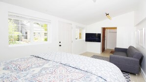 A bedroom with a large bed, a grey sofa, a TV on the wall, and a door leading to another room. - Walk to Village & 5C's & Trader Joe's/Private Pool (Claremont)