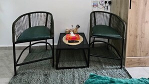A room with two black chairs, a small table with a remote control, a television mounted on the wall, and a wooden wardrobe. - Studio Apartment Near JKIA and SGR (Syokimau)
