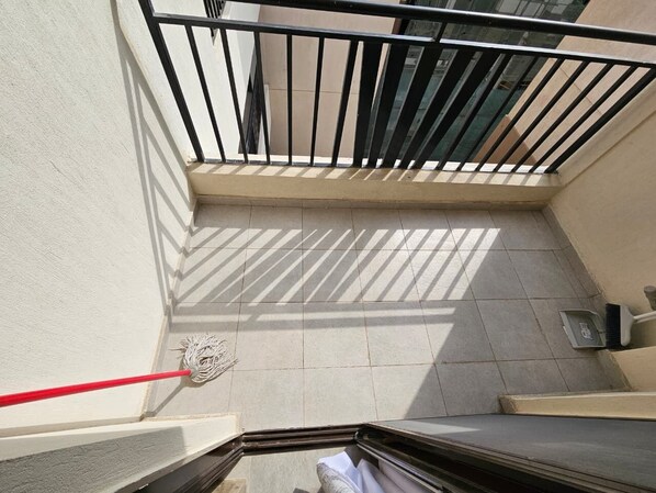A view from a balcony with a tiled floor, a red mop, and a broom leaning against the wall. - Studio Apartment Near JKIA and SGR (Syokimau)