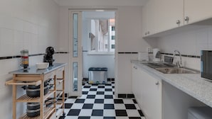 Una cucina compatta con mobili bianchi, pavimento a scacchi bianco e nero e una piccola finestra sullo sfondo.