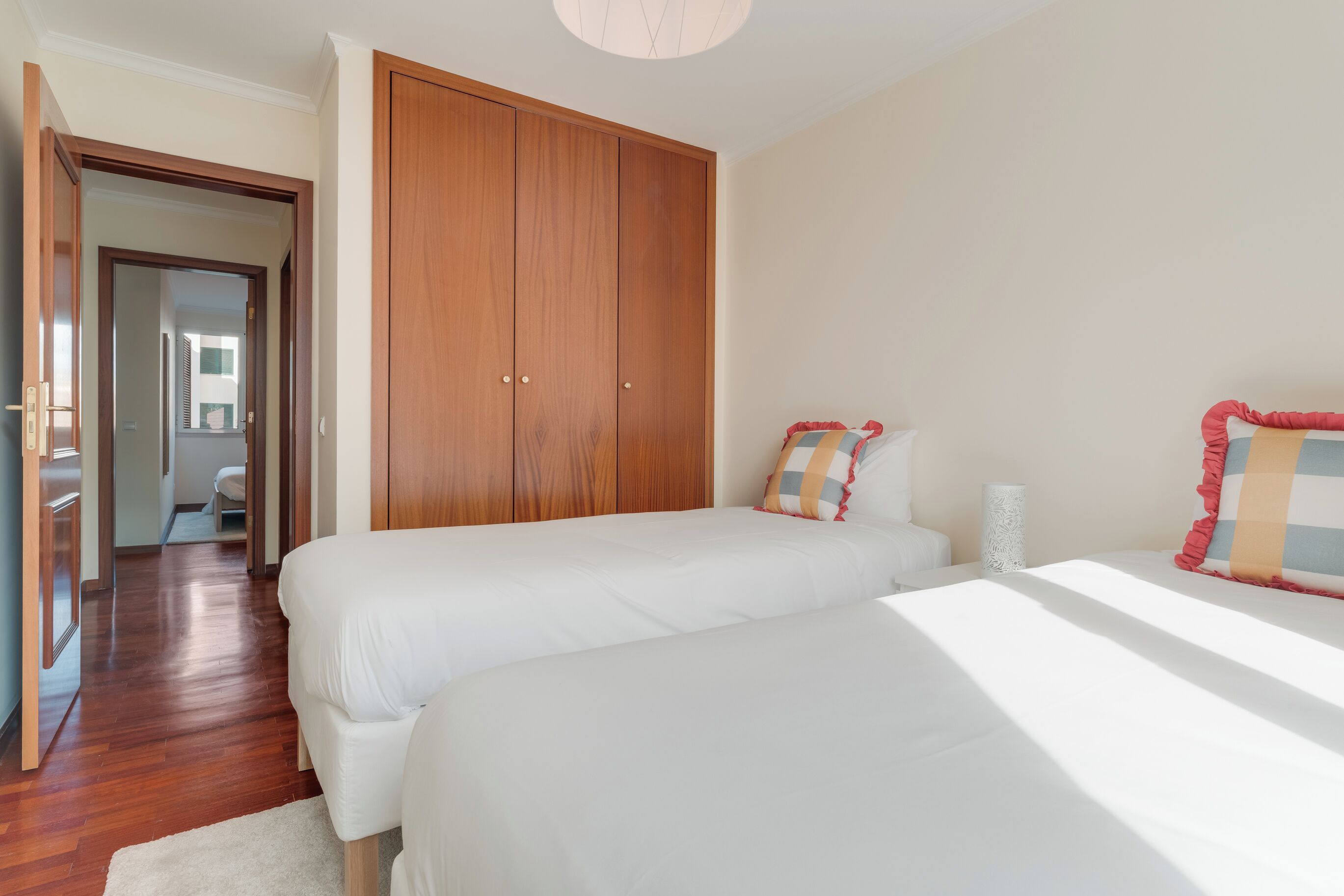 A bedroom with two beds, wooden wardrobe, and a hallway leading to another room.
