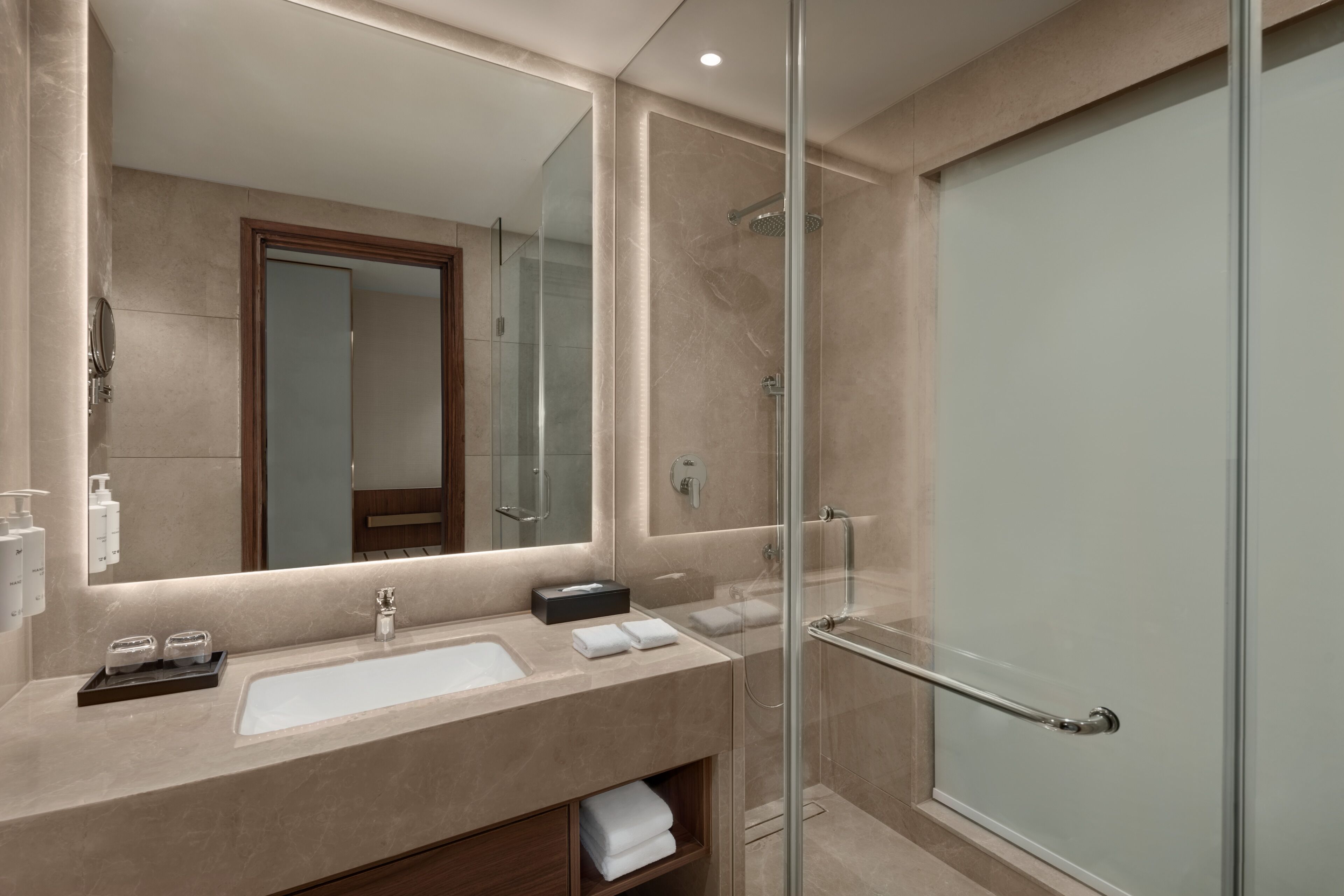 A modern bathroom with a large mirror, a glass shower enclosure, and a beige countertop.