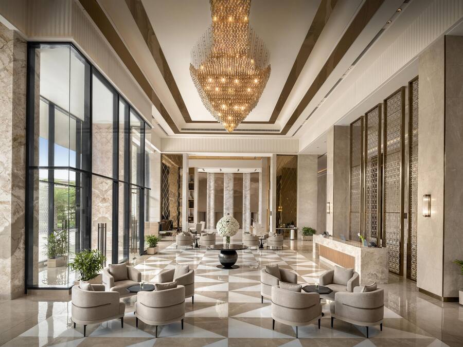A spacious lobby with a large chandelier, marble flooring, and modern seating arrangements.
