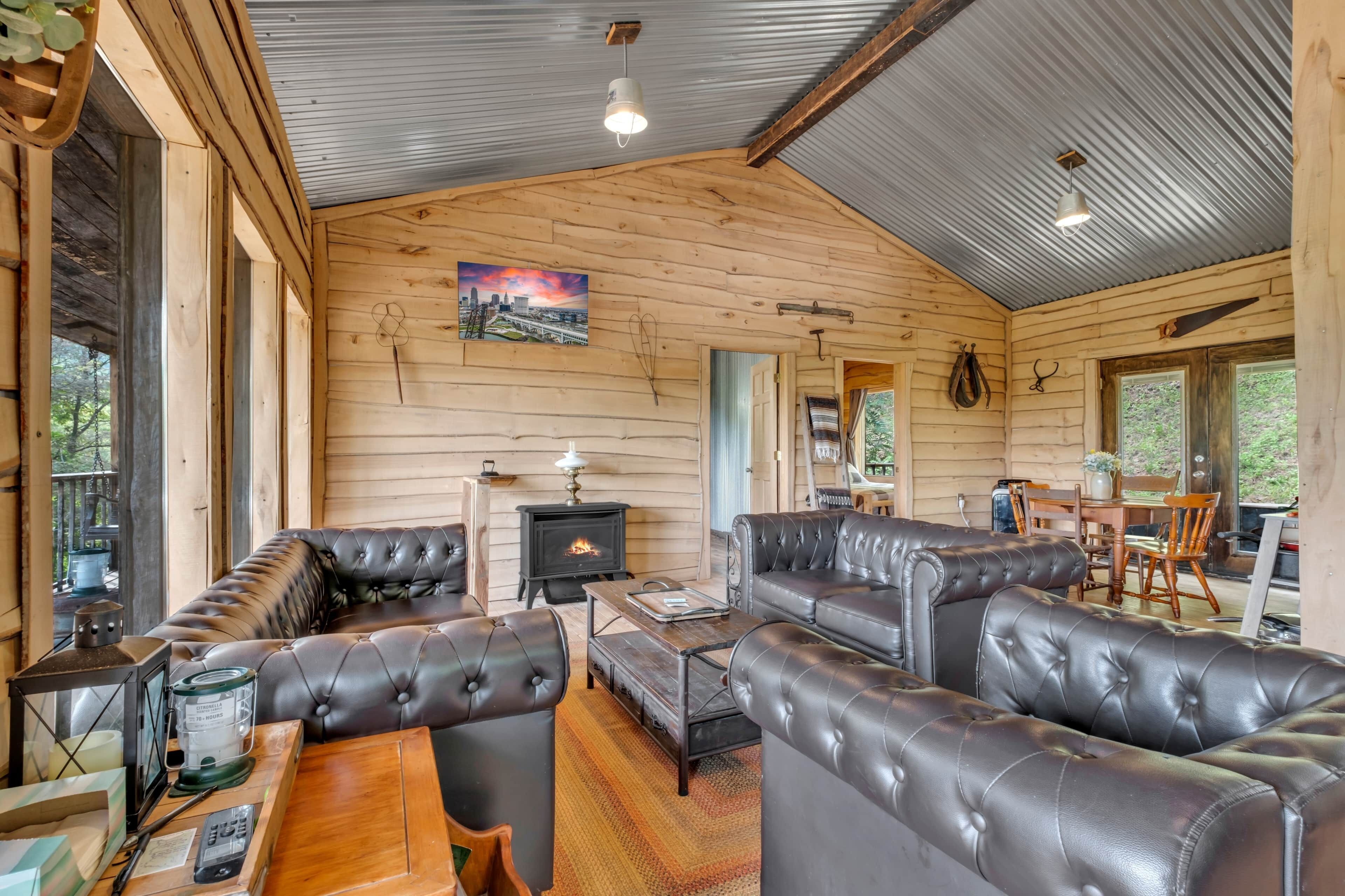 A cozy cabin interior with a fireplace, leather sofas, a dining area, and a large window.