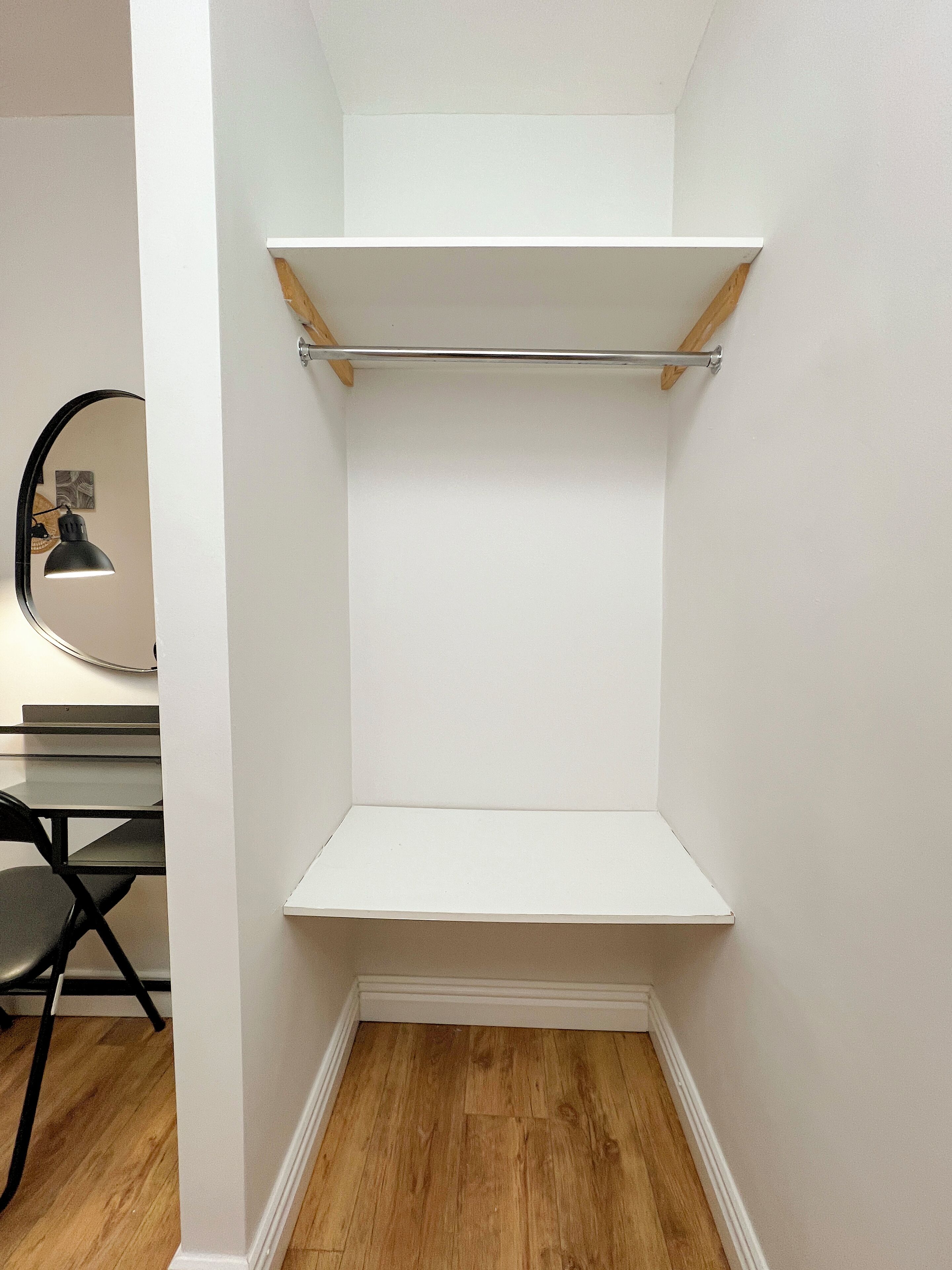 A corner closet with two white shelves and a mirrored closet door.